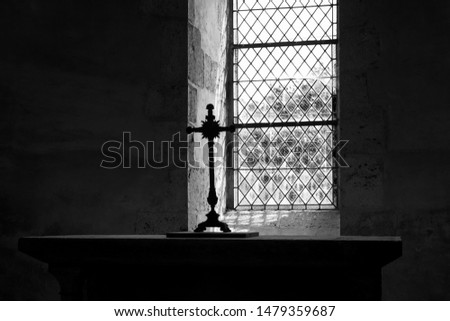 Cross silhouette on altar near window in dark empty old chapel. Game of light and shadow in church. Religious christian background. Despair and hope,  divine mercy, god love concept. Black white photo