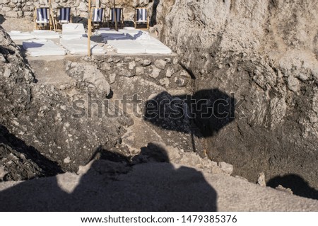 beach club on capri with parasols and mattresses on an underground with stones, sunlight and shadows