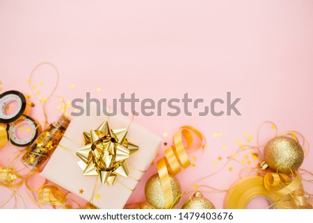 Gift box with golden bow on pink coral background with stars and sparkles. Festive concept copyspace top horizontal view. Sticky tape, Christmas balls, golden ribbon