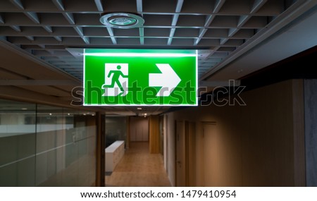 Green fire escape sign hang on the ceiling in the office. Royalty-Free Stock Photo #1479410954