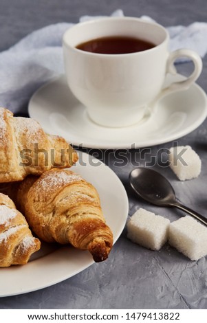 cup of tea, croissants, sugar cubes on a gray background, breakfast concept
