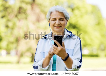 fitness, sport and healthy lifestyle concept - senior woman with earphones listening to music on smartphone at summer park