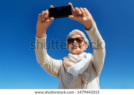 old people and leisure concept - happy smiling senior woman taking selfie by smartphone outdoors over blue sky