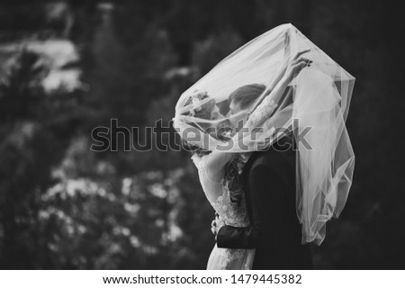 Romantic wedding moment, bride and groom smiles to each other under the veil, happy and joyful moment on nature in the park. Black and white photo.