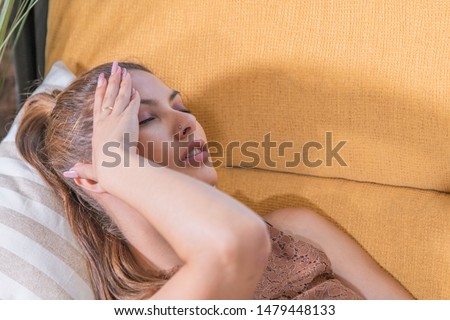 Photo detail of a beautiful and stressed girl lying on the sofa at home, keeps her hand on her head in search of relief. Close-up