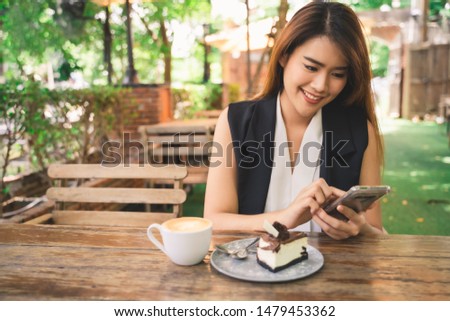 Young attractive happy Asian business woman is using smartphone or tablet with smile face in coffee shop cafe, online shopping content, woman lifestyle background with copy space