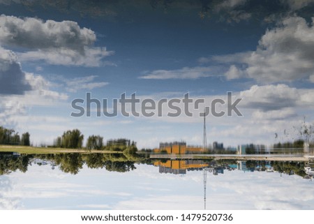 Landscape. Reflection on smooth surface of river of buildings, trees, blue sky and clouds. Symmetry. Inverted picture. Motion blur.