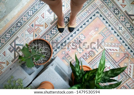 Woman’s perspective of her shoes, plants on floor, vintage pink rug