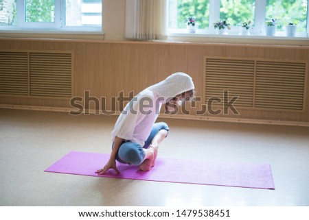Young slim woman in white hood sitting on the yoga mat in lotus position leaning on her toes