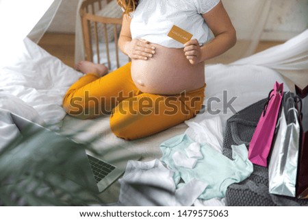 Expectant mother sitting on bed with laptop and doing online shopping stock photo