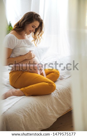 Smiling expectant mother sitting on bed and holding her tummy stock photo