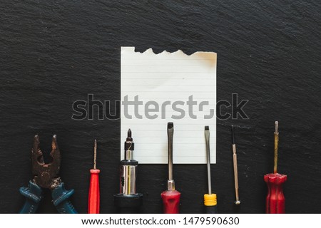 Distinct metal tools aligned in a line on the bottom of the picture with a clear piece of paper. Screwdrivers isolated on a black table background.