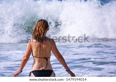 A woman from behind in the waves of the sea