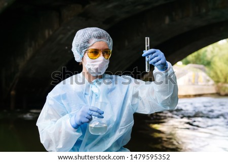 female ecologist examines a test tube with water from a city river in an underground collector, holding a flask in her second hand Royalty-Free Stock Photo #1479595352