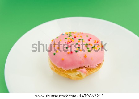 Pink round donut on white plate on green background