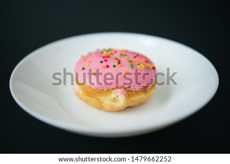 Pink round donut on white plate on black background