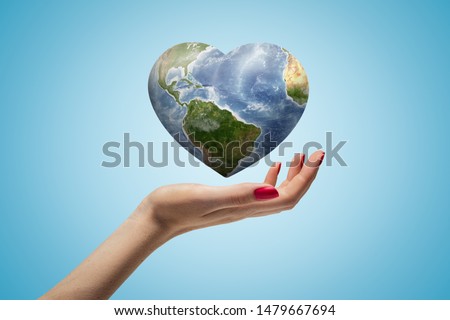 Side closeup of woman's hand facing up and levitating small heart-shaped Earth on light blue gradient background. Promoting peace. Enhancing sustainable development. Nature conservation.