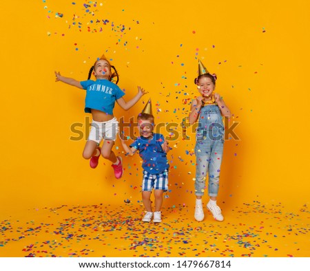 happy children on holidays have fun and  jumping in multicolored confetti on yellow background