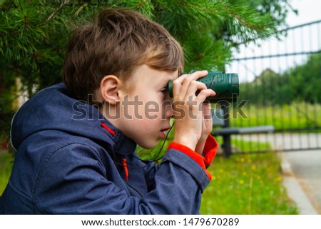The boy watches the Windows of the neighbors. The boy is watching through binoculars.