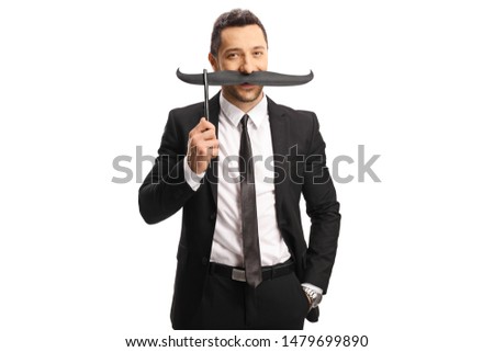 Young man in a suit holding fake mustaches on a stick isolated on white background