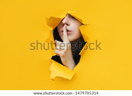 A young girl closes her lips with her index finger,making it clear to the viewer that you need to observe silence,keep a secret and not say too much. Censorship and harassment of freedom of speech. Royalty-Free Stock Photo #1479705314