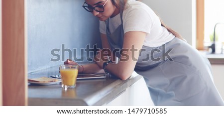 Portrait of young attractive caucasian brunette housewife at kitchen. Morning with cup of coffee and tablet pc