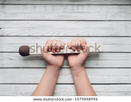 A big match in the hands of a girl on a wooden white background. Concept and photography. Creativity and copy space. Slight inflammation. Human choice.