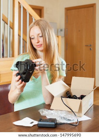 Smiling young  girl unpacking new digital camera  in home interior