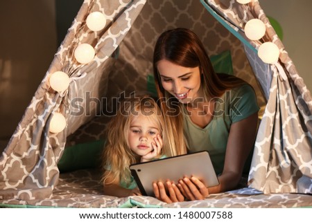 Happy woman and her little daughter with tablet computer in hovel at home
