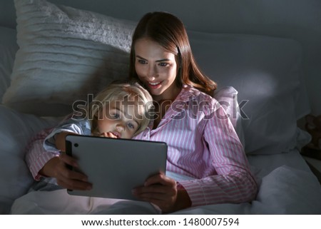 Happy woman with her little daughter with tablet computer in bed