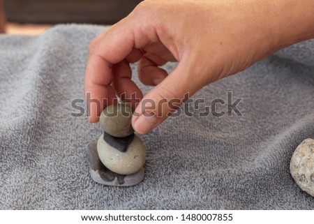 Woman's hand stacks stones on a Terry towel on the beach.