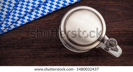 Beer mug with zinc cover on bavarian white and blue fabric and wooden table, top view. Oktoberfest background banner