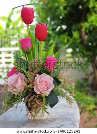 Close up of soft and dark pink roses with red
tulips in the vase. Blurred garden as background.