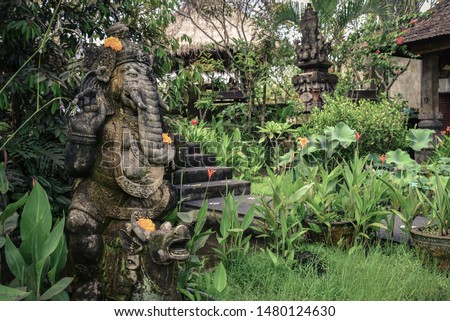 Stone Ganesha statue with orange flowers decorated for religious festival and ceremonial offering, Bali.