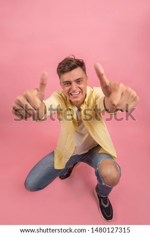 Portrait of a satisfied young man celebrating success isolated over pink background. Photo of handsome man smiling on camera with thumb up 