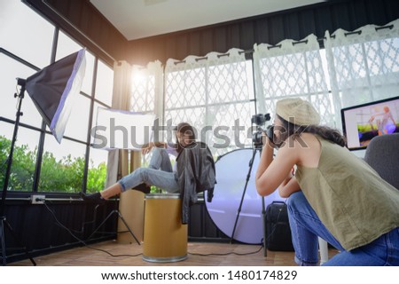 woman freelance photographer and blogger working individual at own office studio with acting of model in background