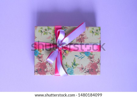 Craft gift box with different beautiful flowers and satin ribbon on the purple background.