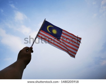 hand holding Malaysia flag wavering in blue sky