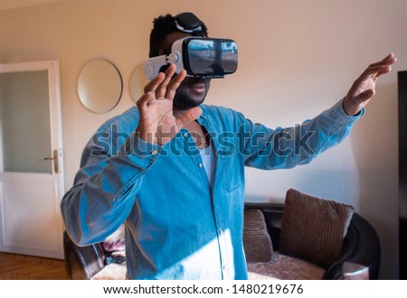 Cool handsome african american man first time wearing virtual reality glasses at home. A man is looking for bright impressions using gadgets.