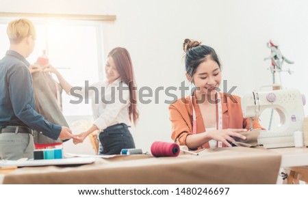 Young dressmaker woman sews clothes on sewing machine. Smiling seamstress and her hand close up in workshop. Focus on sewing machine and tissue.