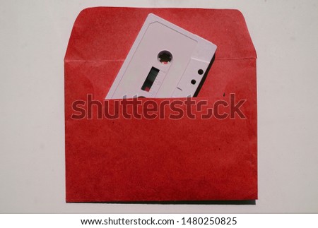 top view of gray audio cassette inside red envelope made from craft paper. isolated on white background. 