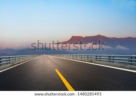 An asphalt road leading to the misty peaks of Rizhao Mountain in the distance Royalty-Free Stock Photo #1480285493