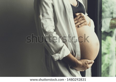Young pregnant women standing near window show her body.