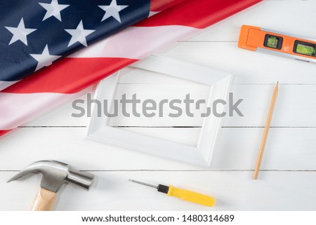 Top view of handy tools, white photo frame and American flag on white wooden background. Happy Labor Day.