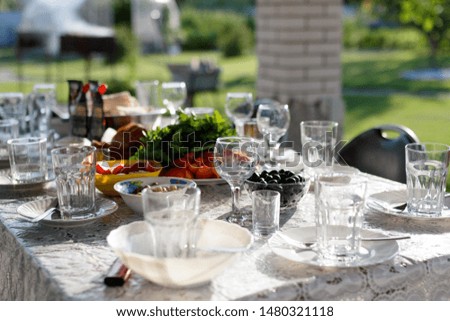 Served table with glasses, plates, spoons, forks. In the plates are vegetables and olives. Outdoor lunch in the summer
