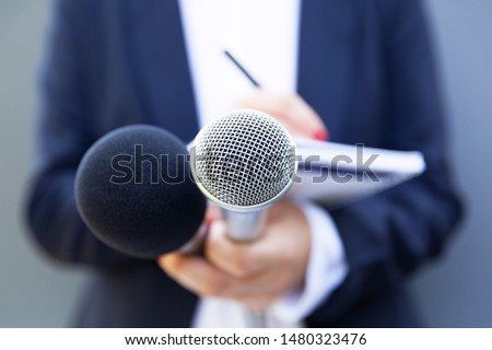 Female journalist at news conference or media event, writing notes, holding microphone Royalty-Free Stock Photo #1480323476