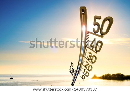 Background for a hot summer day or a heat wave, beach with people, bright sun and a big thermometer
