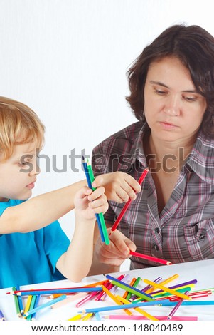 Young mother teaches her son to draw with color pencils on a white background