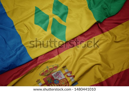 waving colorful flag of spain and national flag of saint vincent and the grenadines. macro