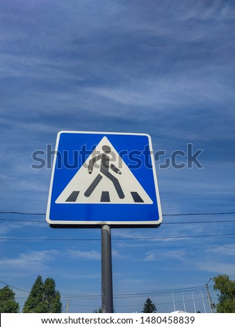 Road sign - Pedestrian crossing. Square blue and white metal plate with white stripes and a walking man. Blue sky background.